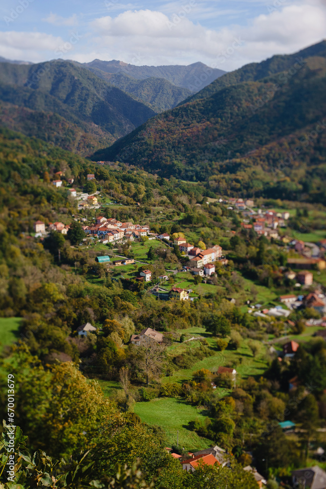 Panoramic view from above, from the throne to the valley in the mountains. A small village in the Alps. Colored houses, tiled roofs, a road and a river. Europe. Italy