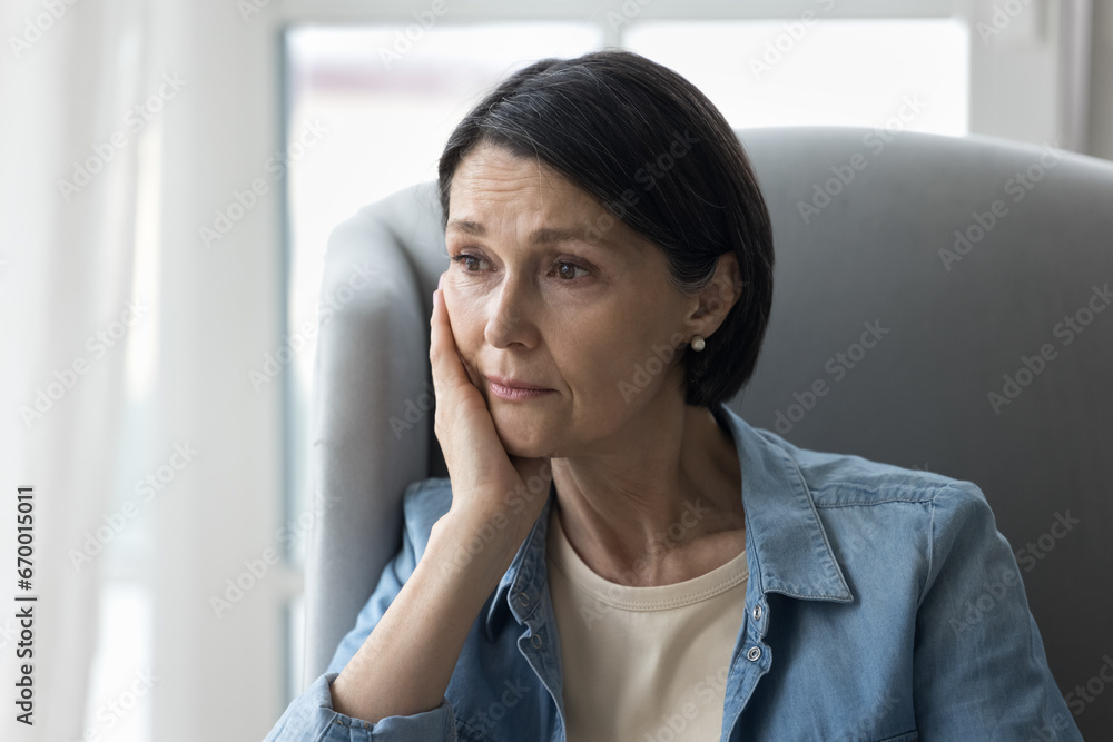 Close up attractive sad worried middle-aged woman sits indoors, staring aside and thinking, suffers from melancholy or solitude, goes through divorce. Break up, life troubles, stressful situations Close up attractive sad worried middle-aged woman sits indoors, staring aside and thinking, suffers from melancholy or solitude, goes through divorce. Break up, life troubles, stressful situations