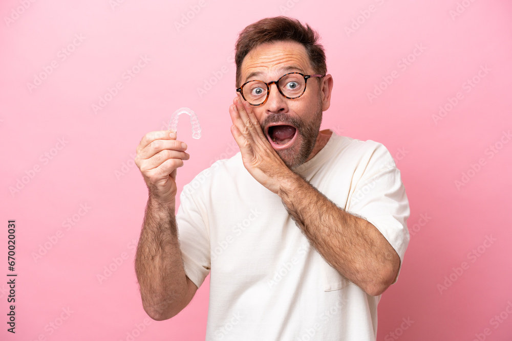 Middle age man holding invisible braces isolated on pink background whispering something - obrazy, fototapety, plakaty 