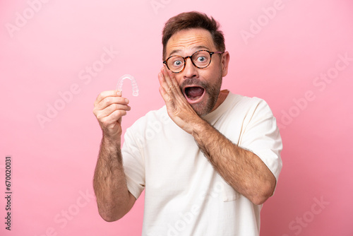 Middle age man holding invisible braces isolated on pink background whispering something photo