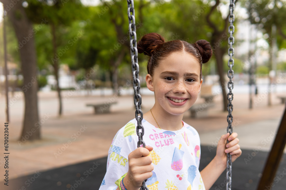 Portrait of a red haired girl with freckles looking at camera laughing while she swings at a playground. Happiness and joy concepts Portrait of a red haired girl with freckles looking at camera laughing while she swings at a playground. Happiness and joy concepts