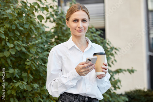 Pretty young woman with white hair dressed in a white shirt drinks coffee while sitting on the street