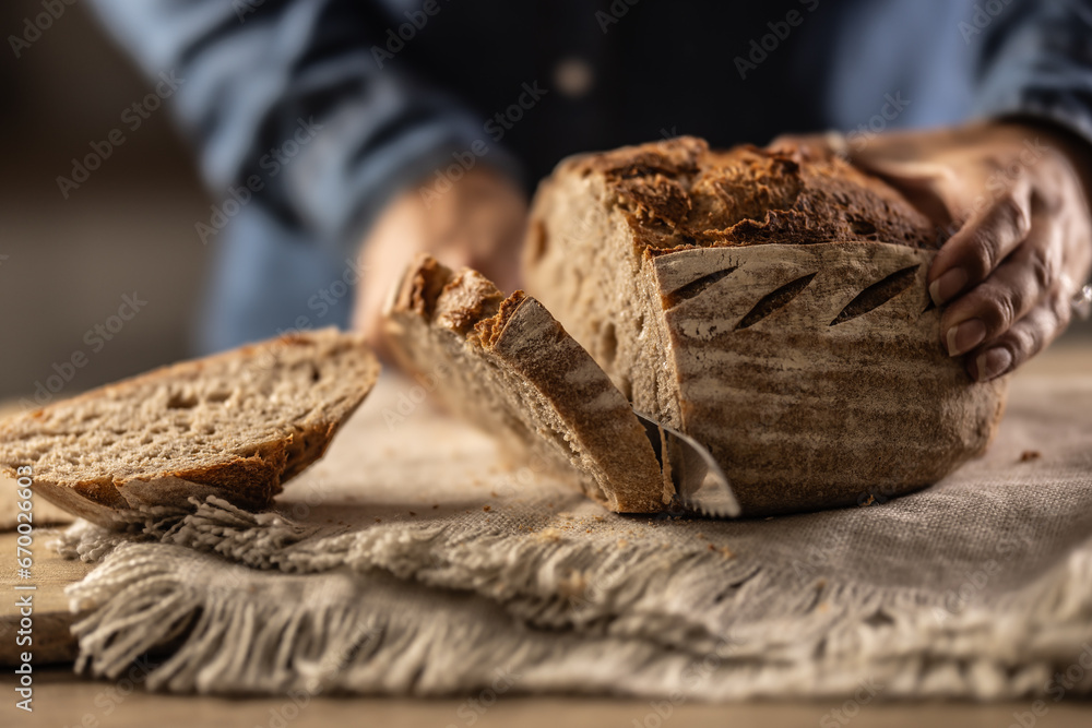 Woman cutting fresh bread on counter in kitchen - close up.