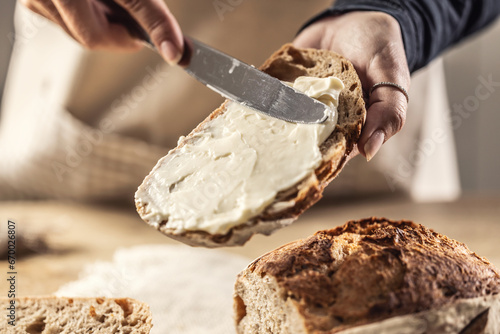 A woman makes delicious bread, spreads cream cheese with a cutlery knife - Close up. Woman hands spreading cream cheese on bread slice.