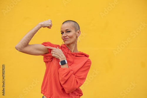 Shaved head woman flexing muscles in front of yellow wall photo
