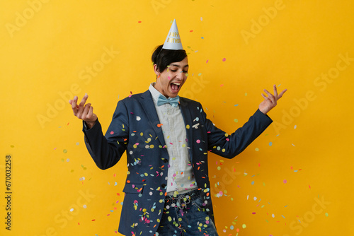 Joyful young man with party hat throwing confetti in studio photo