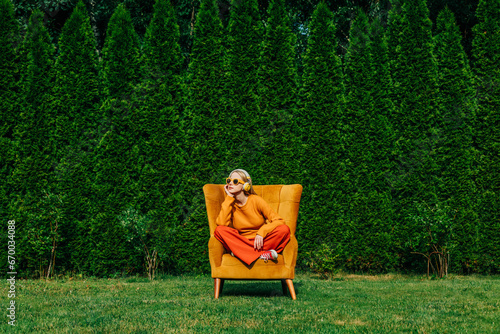 Blond woman sitting on armchair in garden