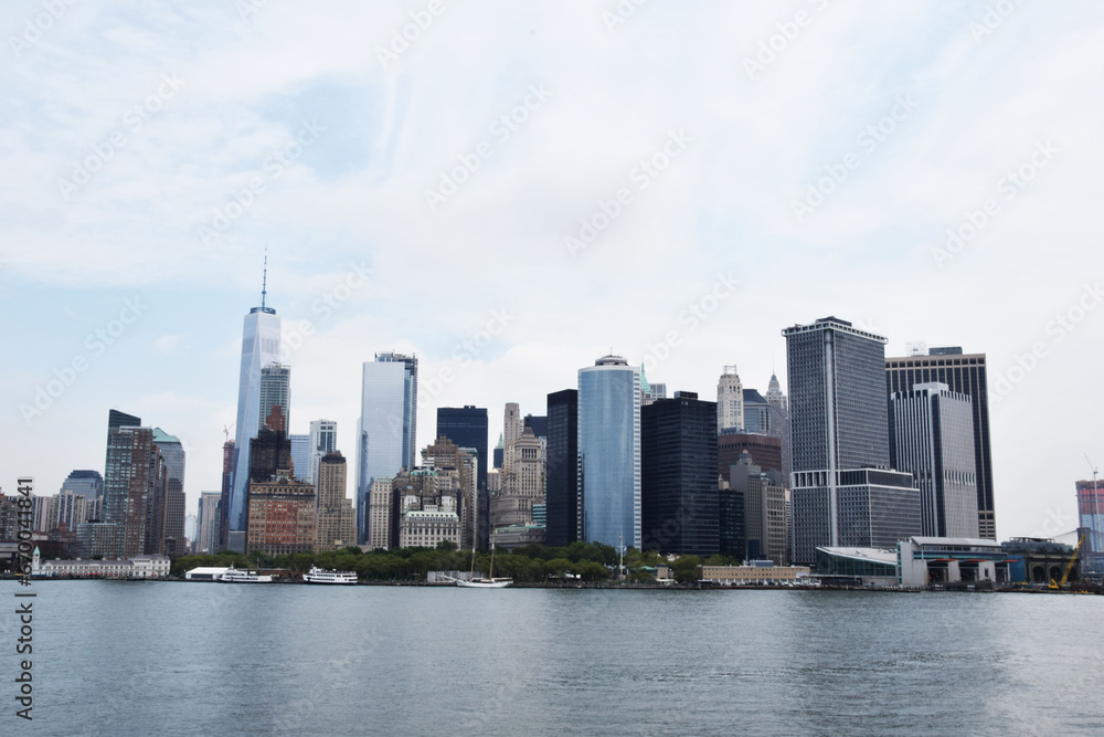 Skyscrapers of manhattan located near rippling water of new york bay against cloudy blue sky