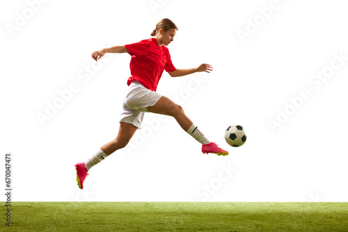 Athletic young woman, football player in motion during game, hitting ball on grass field isolated on white background. Concept of sport, competition, action, success, motivation. Copy space for ad © master1305
