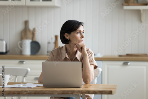 Konstfotografi Serious middle-aged woman sit at table in kitchen with laptop, working, managing