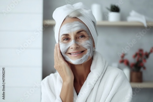 A beautiful elderly gray-haired woman with a cosmetic nourishing moisturizing mask on her face smiles on gray background. Facial skin care concept, beauty, care, cosmetology photo