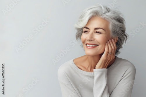 Portrait of beautiful mature woman with snow-white smile  gray hair on gray background. Middle-aged lady in light clothes  happy pensioner looking at the camera. Beauty  skin care concept