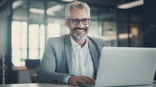 Mature smiling businessman working on laptop computer in office. © Muhammad_Waqar