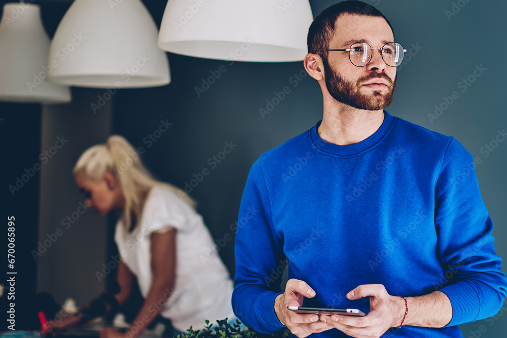 Fotografie Pensive caucasian hipster guy in casual wear sitting on frontage with portable p