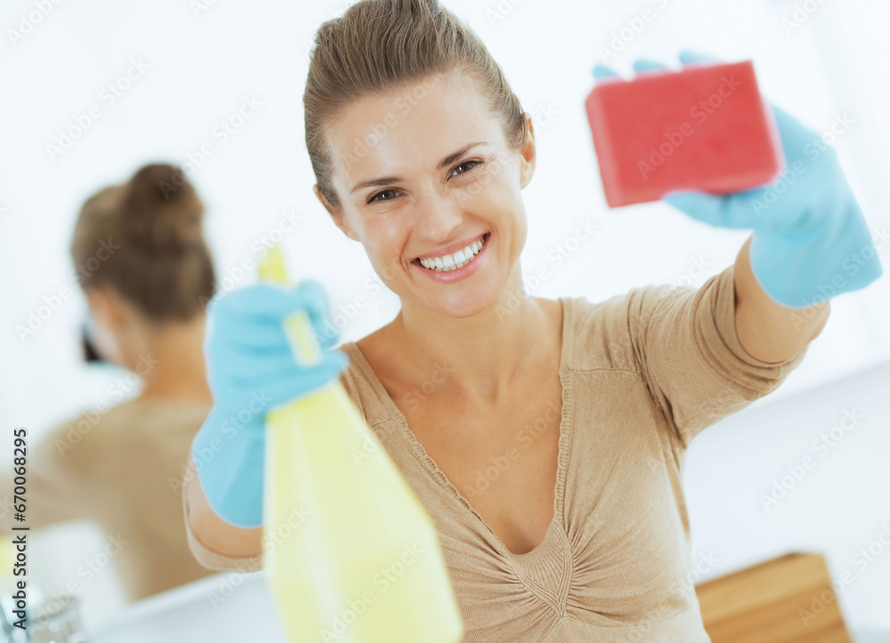 Happy young housewife showing spray bottle and sponge Happy young housewife showing spray bottle and sponge