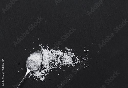 Organic sea white salt and a spoon on a black slate background. Concept of cooking natural healthy food photo