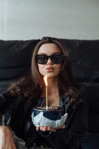 Fashionable attractive woman with cake in hands blowing out birthday candle. Fashion portrait of the birthday girl.