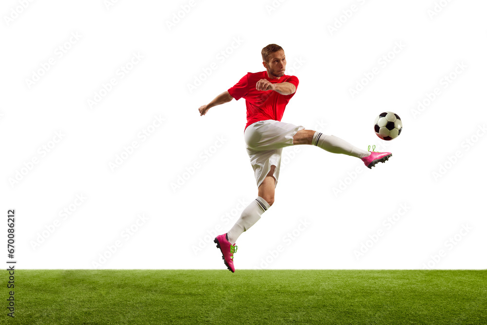 Full length portrait of professional soccer player kicking ball against white background on green grass. Looks extremely motivated.
