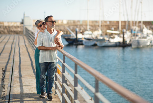 Mature spouses enjoying embrace near ships and yachts at marina