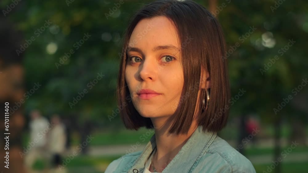 Beautiful young woman standing outdoor smiling and looking at camera. Portrait of attractive female posing with happy smile in golden hour Beautiful young woman standing outdoor smiling and looking at camera. Portrait of attractive female posing with happy smile in golden hour