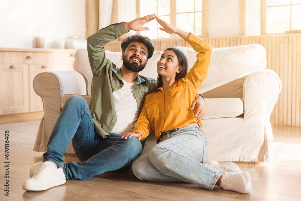 Couple forming a roof shape with hands, sitting at home