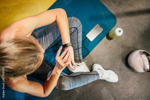 Young fit and attractive woman sitting and resting after fitness workout. She uses her wrist sport band or watch to track fitness data and accomplishments.