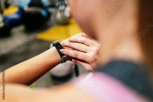 Young fit and attractive woman sitting and resting after fitness workout. She uses her wrist sport band or watch to track fitness data and accomplishments.