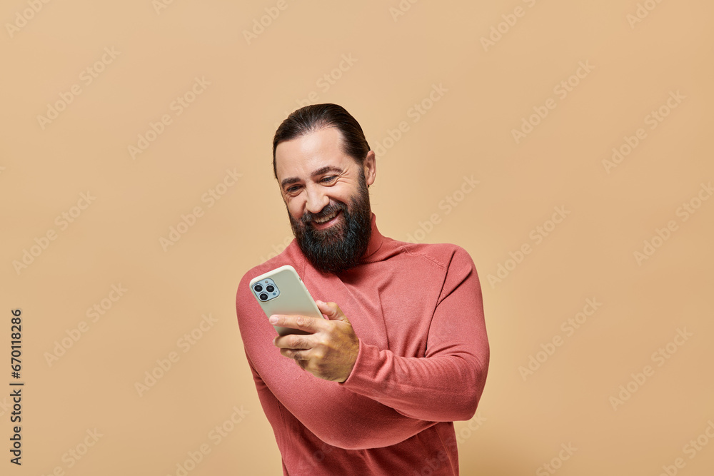 portrait of cheerful bearded man in turtleneck jumper holding smartphone on beige background portrait of cheerful bearded man in turtleneck jumper holding smartphone on beige background