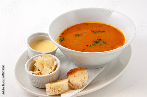 Fresh tomato soup in a bowl with bread, cream and parmesan cheese.