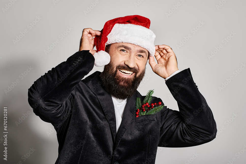 portrait of cheerful handsome man in elegant suit wearing santa hat on grey backdrop, Christmas portrait of cheerful handsome man in elegant suit wearing santa hat on grey backdrop, Christmas