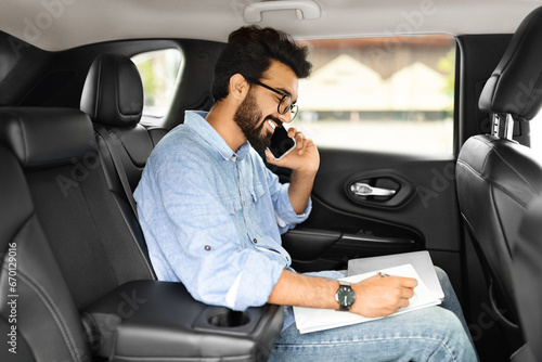 Smiling young indian businessman talking over phone, sitting in taxi © Prostock-studio