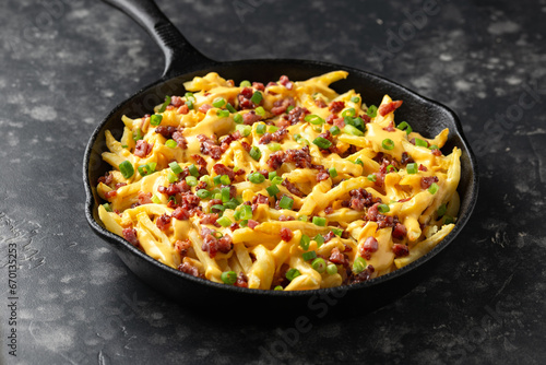 Crispy French fries loaded with bacon, cheese sauce and spring onion in iron cast pan
