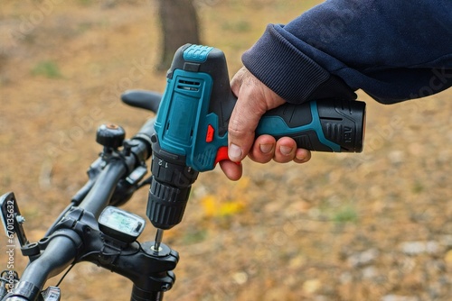 electric modern portable battery powered manual convenient blue plastic powerful screwdriver tool in the hand of a worker when unscrewing a bolt during repair of a sports black mountain bike