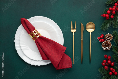 Clean plate, gold cutlery. Festive table setting with christmas decorations. Celebration xmas eve: flat arrangement. Red, golden accents. Fir cones on evergreen tree. Holiday banquet, top view.