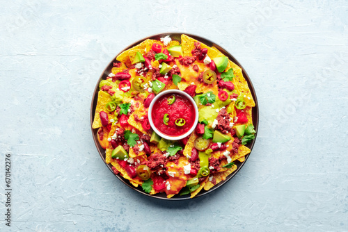 Loaded nachos. Mexican nacho chips with beef, guacamole sauce, cheese salsa, beans and peppers, on a slate background, overhead shot