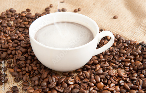 Cup of coffee on a saucer with coffee beans on a background of burlap