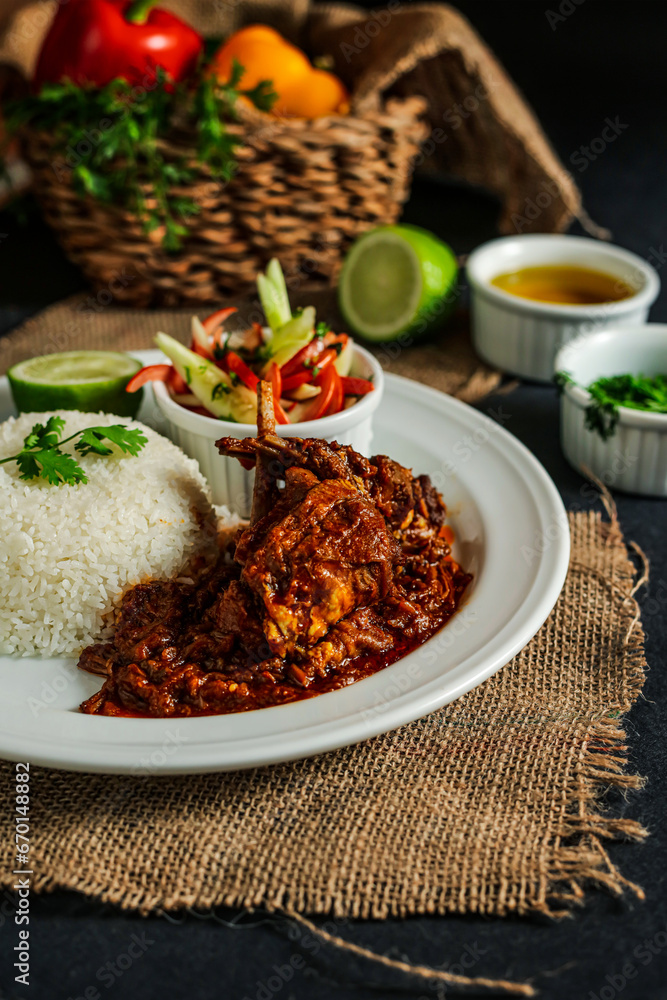 Jamaican Mutton gravy with plain rice, salad, tomato, cucumber dip, sauce and bell pepper served in plate isolated on napkin side view of lunch food Jamaican Mutton gravy with plain rice, salad, tomato, cucumber dip, sauce and bell pepper served in plate isolated on napkin side view of lunch food