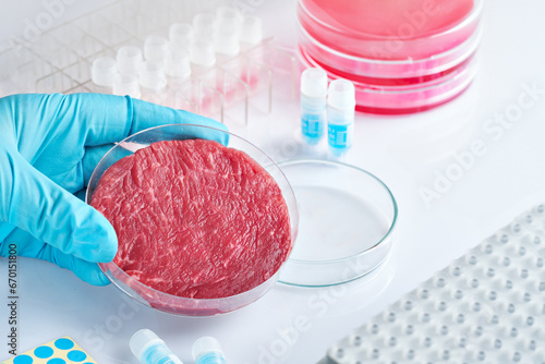 Fényképezés Hand in blue glove holding a petri dish with artificial meat, vat produced meat using cell culture