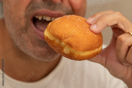 man eating Bola de Berlim or Berlim Ball, a Portuguese pastry made from a fried donut filled with sweet cream photo