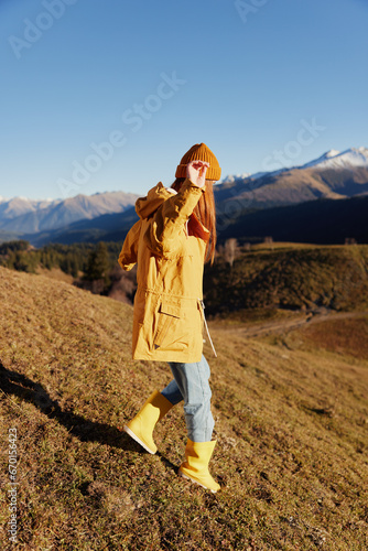 Woman back full-length walks on a hill and looks at the mountains in a yellow raincoat and jeans in the autumn happy trip in the sunset sunset hiking, freedom lifestyle  © SHOTPRIME STUDIO