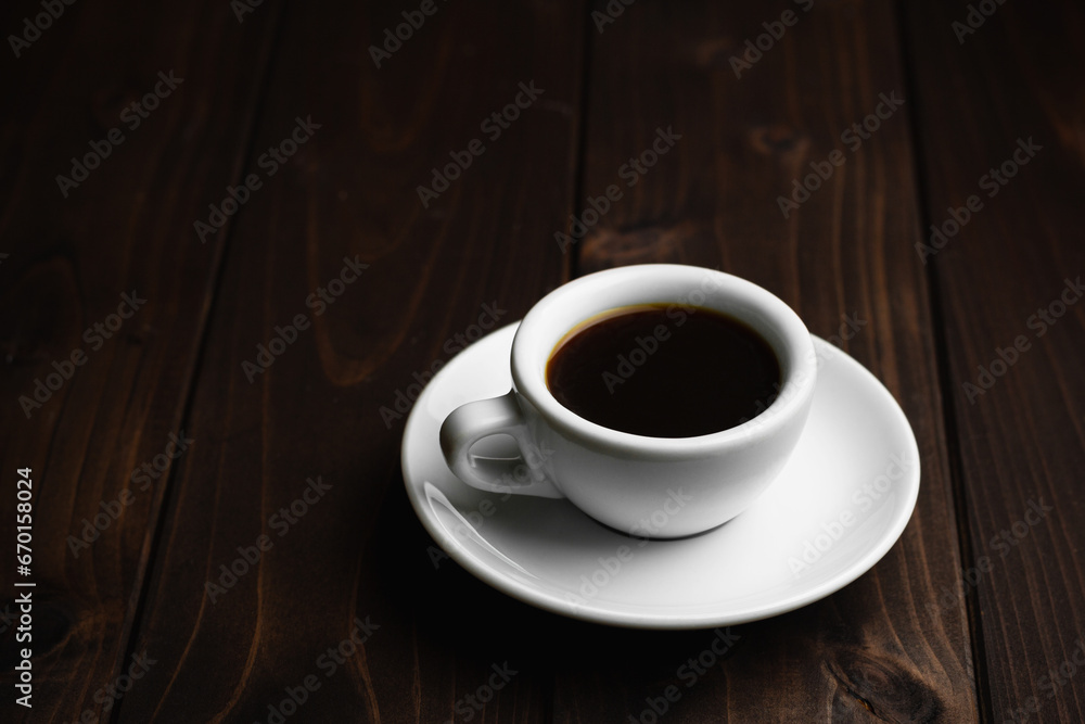 Obraz premium Close up white coffee cupon black wood table with light shade on tabletop at cafe.