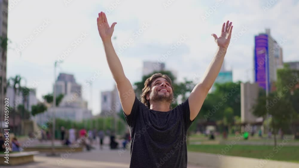 Exultant Young Man Expressing Hope and Faith with Uplifted Arms Celebrating Triumph Outdoors in the Park Exultant Young Man Expressing Hope and Faith with Uplifted Arms Celebrating Triumph Outdoors in the Park