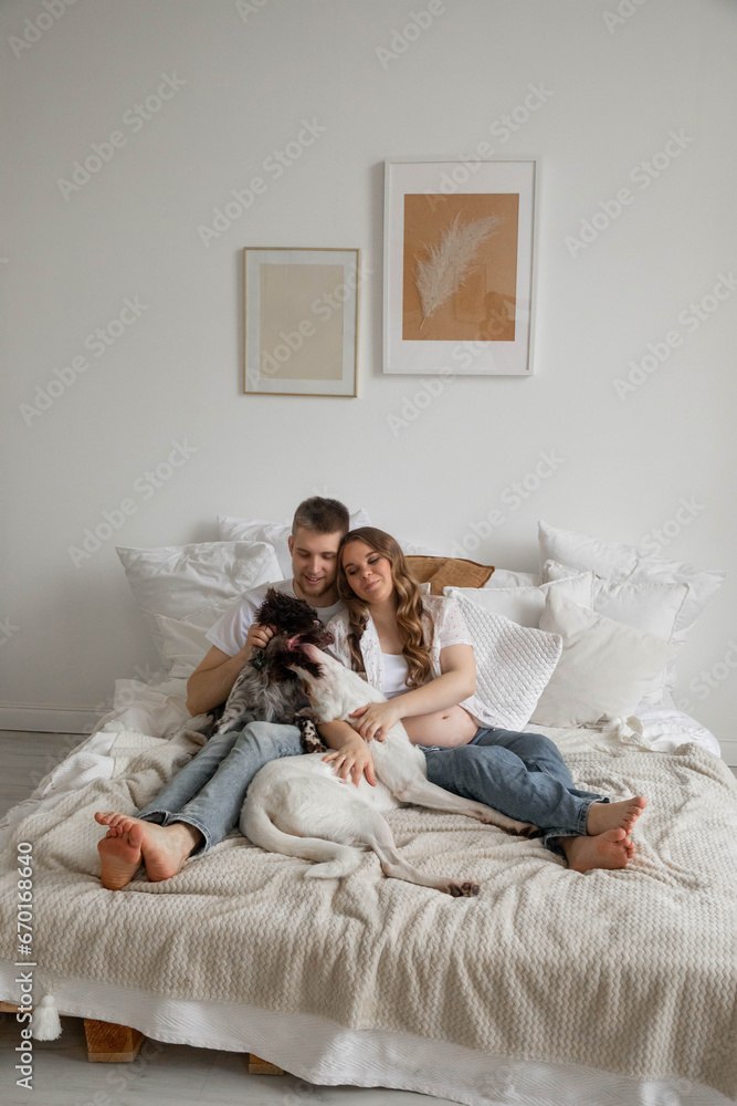 Couple in love, pregnant girl and guy with dogs on bed, bright photo Couple in love, pregnant girl and guy with dogs on bed, bright photo