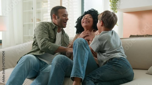 Laughing happy multiracial family playing with child funny game on couch at home playful dad and little kid son boy tickling mom fun laugh carefree parents ticklish laughter weekend bonding together