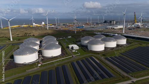 Solar panel park with windmills and fuel silos and harbor in background, Aerial