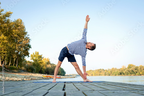 Active man practicing young on the pier by the river