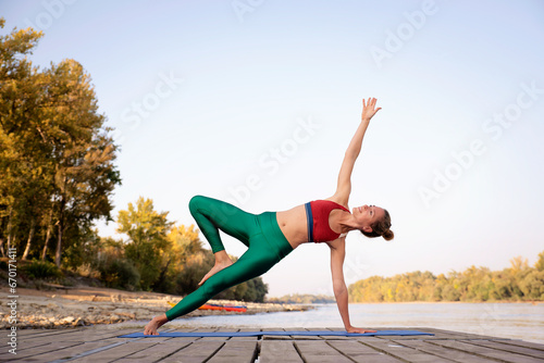 Full length of a woman practicing yoga on the pier on riverside