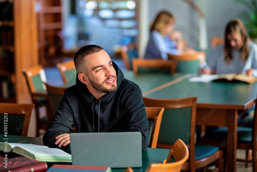 Confident male university student sitting in the library and studying Confident male university student sitting in the library and studying
