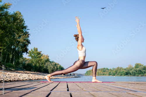 Full length of a woman practicing yoga in summer on a jetty at a lake