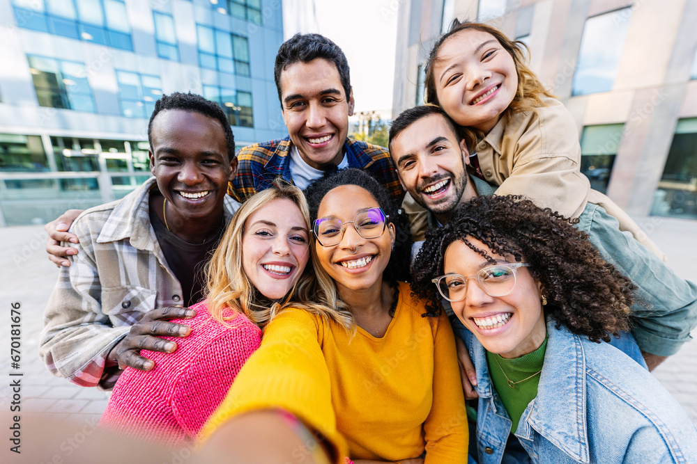 Diverse student group enjoying time together taking selfie portrait with cell phone app outdoors. United multiracial friends laughing and having fun at city street. Friendship and youth concept. Diverse student group enjoying time together taking selfie portrait with cell phone app outdoors. United multiracial friends laughing and having fun at city street. Friendship and youth concept.